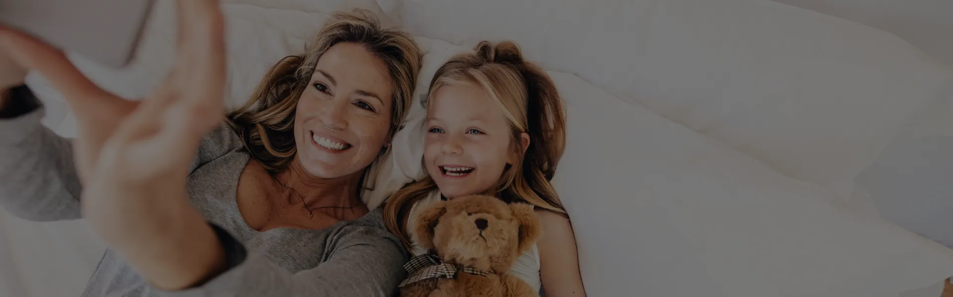 Mother and daughter smiling in bed with a teddy bear