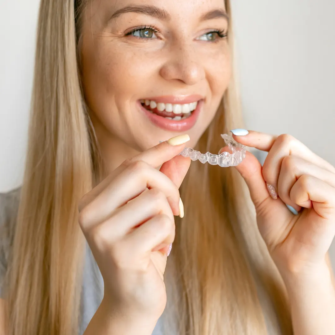 Woman smiling while holding a clear aligner